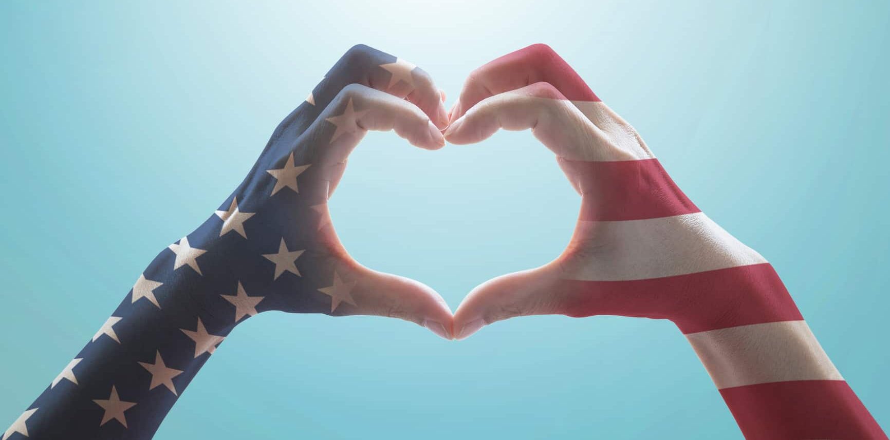 American flag pattern on people hands in heart shaped form against vintage sky background w/ clouds: shows how Valor Elite supports first responders